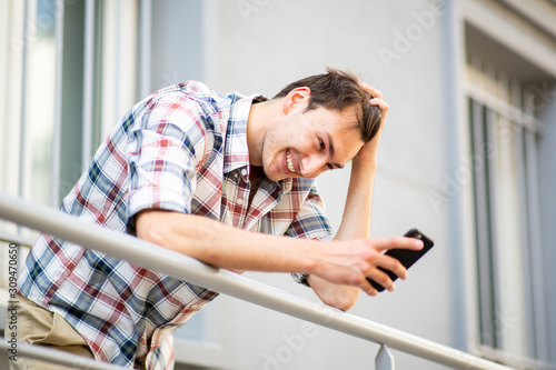 happy young man on balcony looking at mobile phone