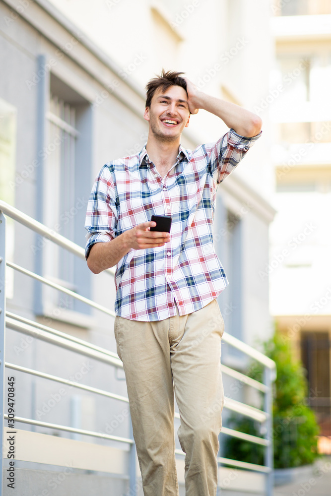 Fototapeta premium happy young guy walking with cellphone outside