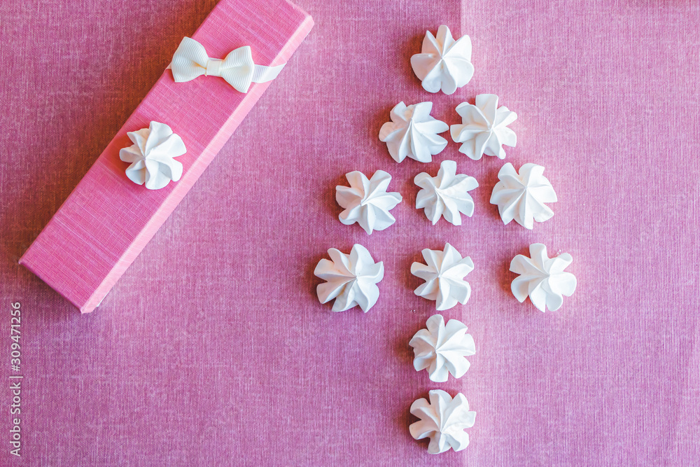 Alternative Christmas tree of meringues on a background of pink fabric next to a gift box with a bow. Copy space. Alternative Christmas tree of meringues on a background of pink fabric next to a gift box with a bow. Copy space.