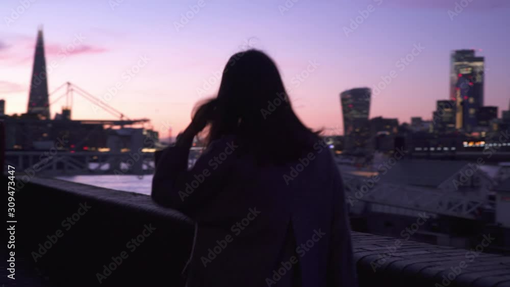 Tourist female walking alongside London Thames river with City of London skyline view at dusk Tourist female walking alongside London Thames river with City of London skyline view at dusk