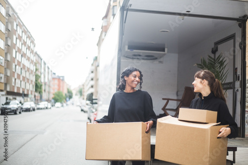 Smiling female movers unloading boxes from truck on street in city photo