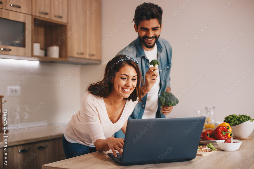 A girlfriend and a boyfriend video chatting with someone while preparing food in the kitchen. A girlfriend and a boyfriend video chatting with someone while preparing food in the kitchen.