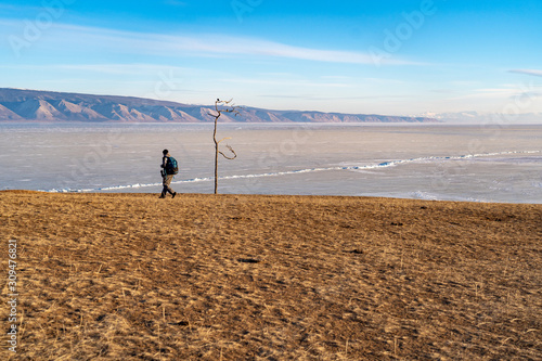 travel man and old dry tree on the sand on icy lake ice and mountains