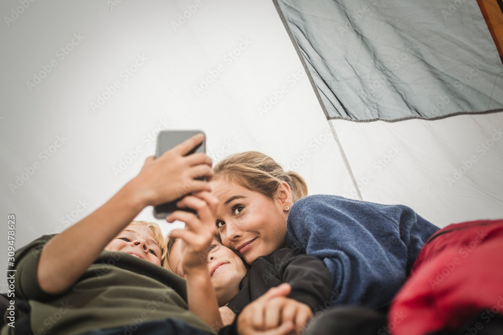 Boy taking selfie with sisters while lying in tent Boy taking selfie with sisters while lying in tent