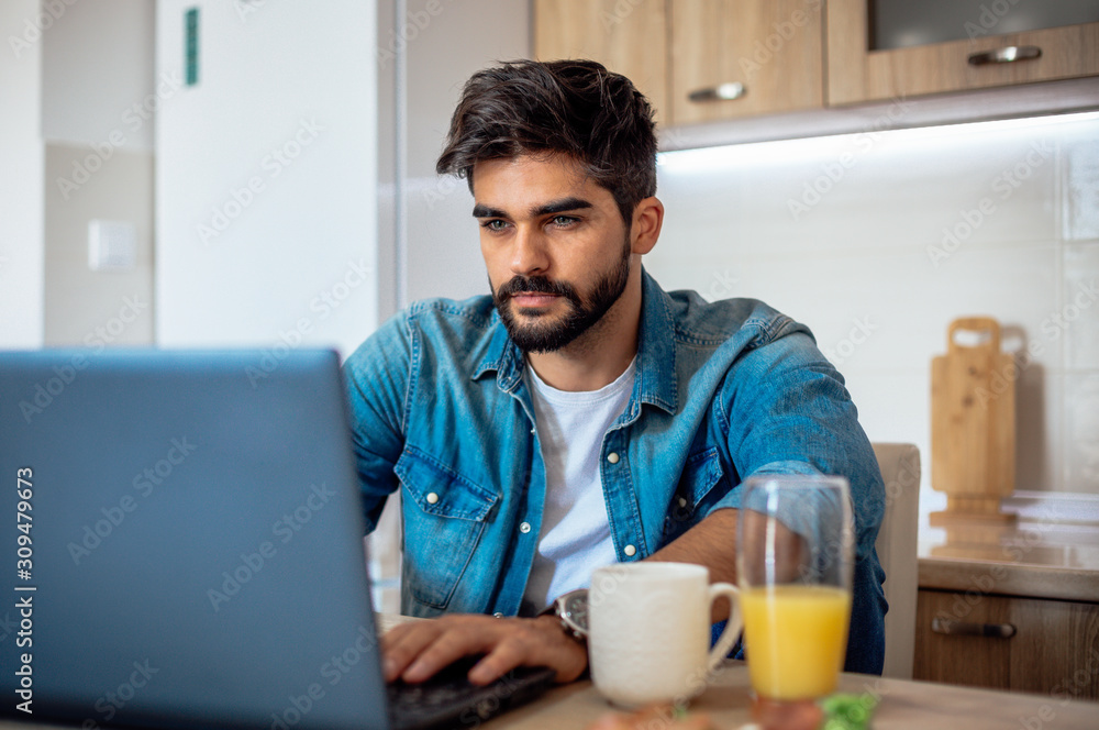 Young handsome entrepreneur checking his emails over the breakfast while sitting in the kitchen. Young handsome entrepreneur checking his emails over the breakfast while sitting in the kitchen.