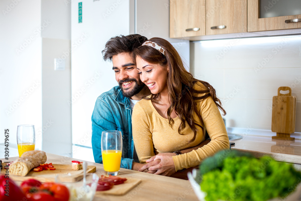 Young good-looking Caucasian couple in love embracing and enjoying their meal together while they are sitting in the kitchen. Young good-looking Caucasian couple in love embracing and enjoying their meal together while they are sitting in the kitchen.