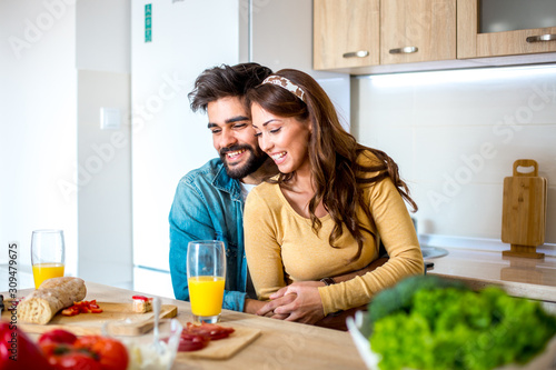 Young good-looking Caucasian couple in love embracing and enjoying their meal together while they are sitting in the kitchen.