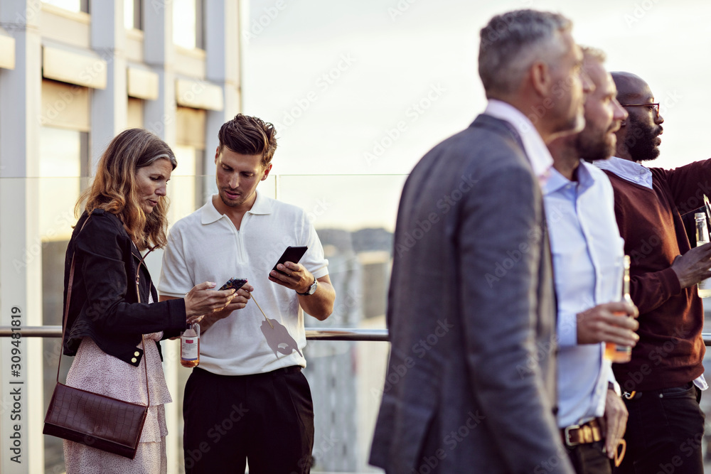 © Maskot - Professionals talking over smart phones while colleagues enjoying in office party after work © Maskot - Professionals talking over smart phones while colleagues enjoying in office party after work