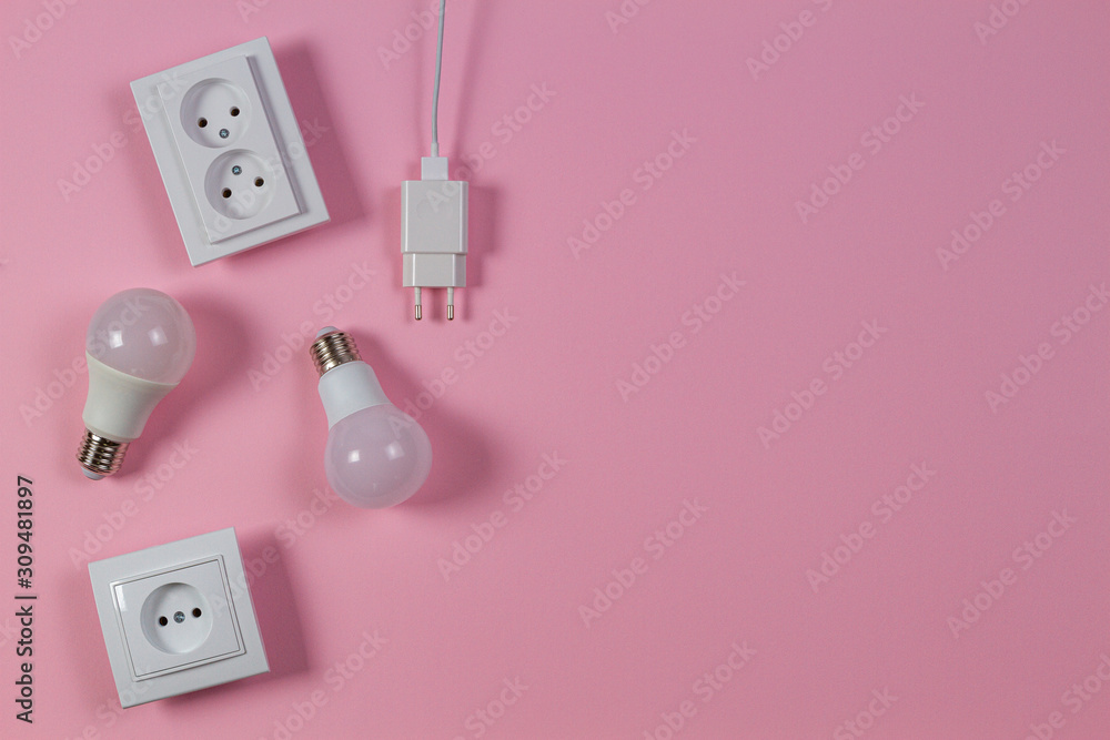 Fototapeta premium White electrical power sockets, power plugs, light lamp bulbs on light pink background. Top view