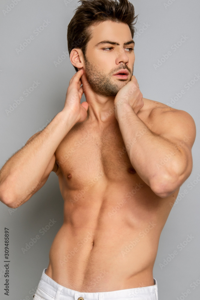 Muscle strong face beautiful stripped male model portrait in white denim jeans on grey isolated font background with shadow Muscle strong face beautiful stripped male model portrait in white denim jeans on grey isolated font background with shadow