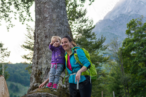 Obraz na płótnie Mother supporting her daughter standing on tree trunk exploring the forest view in mountains. w salonie