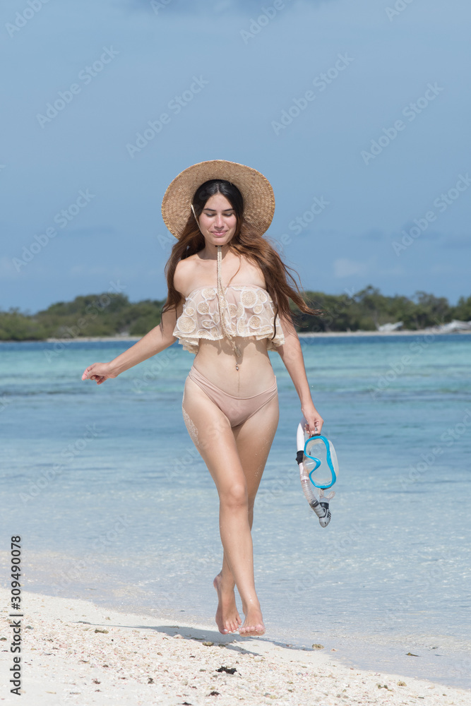 Young happy woman with wet skin, hat and snorkel walking on sand beach 