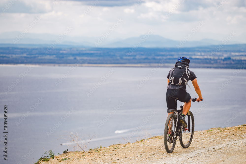 young guy riding a mountain bike on a bicycle route in Spain. Athlete on a mountain bike rides off-road against the background of the Mediterranean Sea, Costa Brava. Cycling in Spain young guy riding a mountain bike on a bicycle route in Spain. Athlete on a mountain bike rides off-road against the background of the Mediterranean Sea, Costa Brava. Cycling in Spain