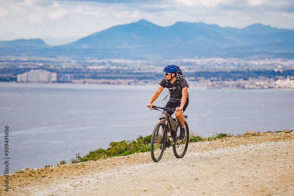Fototapeta premium young guy riding a mountain bike on a bicycle route in Spain. Athlete on a mountain bike rides off-road against the background of the Mediterranean Sea, Costa Brava. Cycling in Spain