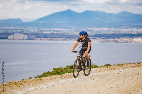 young guy riding a mountain bike on a bicycle route in Spain. Athlete on a mountain bike rides off-road against the background of the Mediterranean Sea, Costa Brava. Cycling in Spain