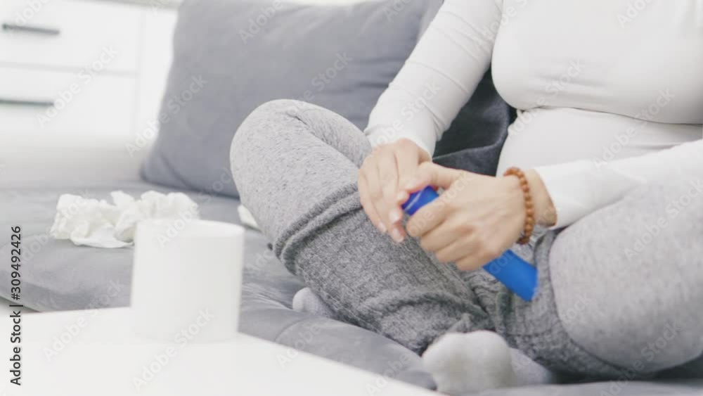 Pregnant woman catching cold, flu, virus, sitting at home on a couch, using tablet in the cup and being sick. Pregnant woman catching cold, flu, virus, sitting at home on a couch, using tablet in the cup and being sick.