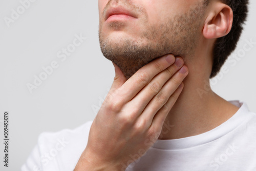 Close up of sick man suffering from throat problems, grey background, isolated. Thyroid gland, painful swallowing, pharyngitis, laryngeal swelling concept. Inflammation of the upper respiratory tract photo