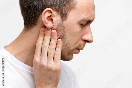 Close up portrait of sick man touches the lymph nodes with his fingers near the ear, suffering from pain, closed eyes, isolated. Lymphadenitis, immunity weakened after illness. Copy space.  photo