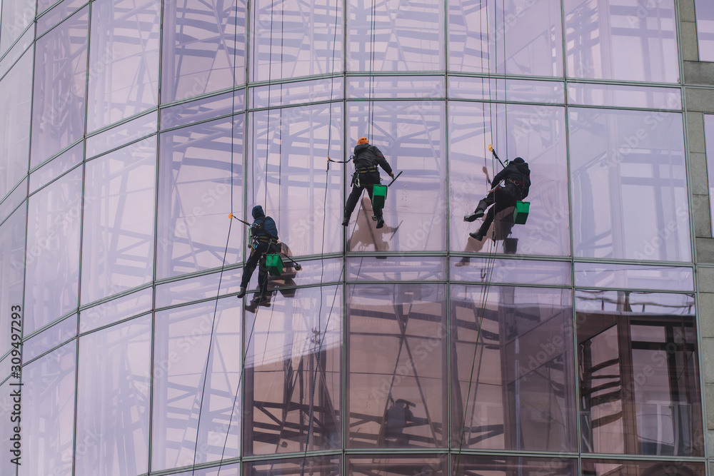 Group of workers cleaning the windows on the high rise building, industrial mountaineers washing the glass facade of a modern office building Group of workers cleaning the windows on the high rise building, industrial mountaineers washing the glass facade of a modern office building