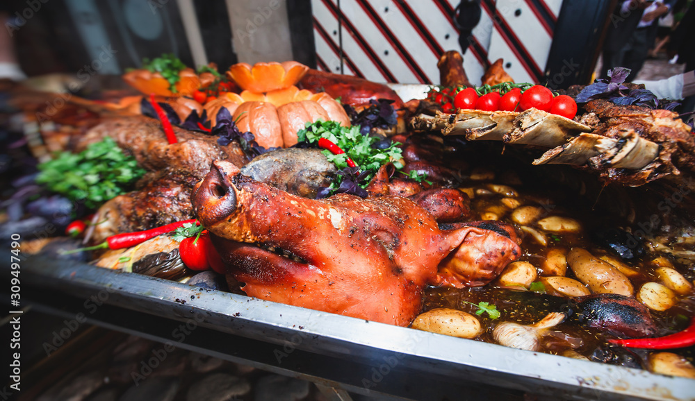 Big giant dish plate with roasted full pig pork head, served in restaurant with variety of vegetables and different meat assortment - lamb, ham and chicken.