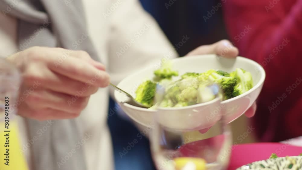 Young man in sweater tasting a salad putting portion on plate sitting with girlfriend at dinner table. Delicious holiday food. Christmas celebration.