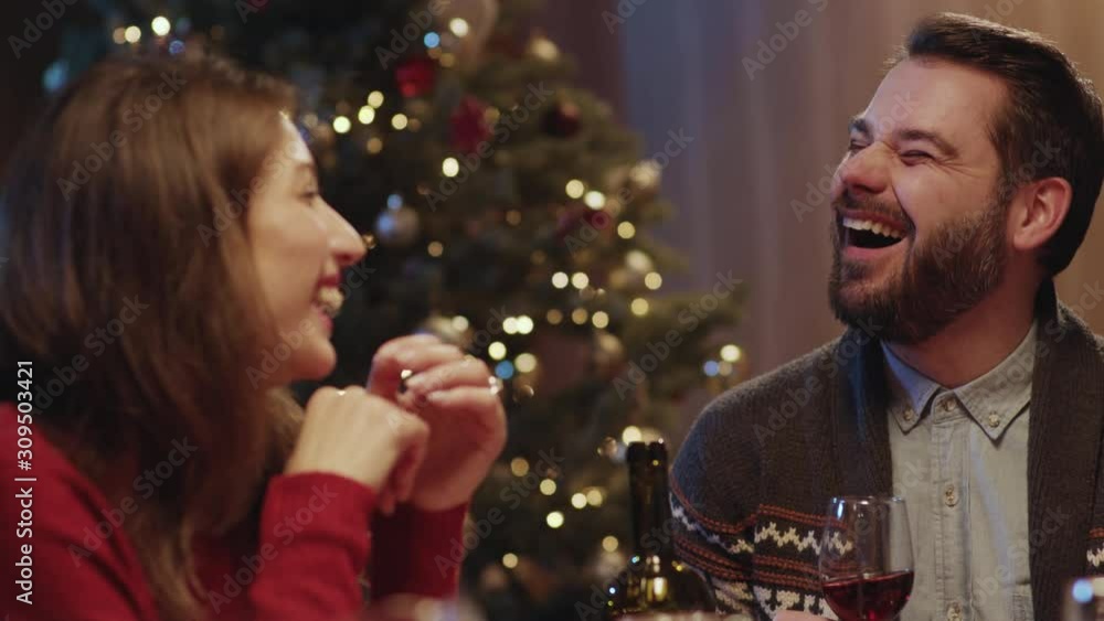 Attractive caucasian people celebrating New Year's Eve at dinner table near Christmas tree. Happy friends laughing together having fun talking enjoying holiday feast. Attractive caucasian people celebrating New Year's Eve at dinner table near Christmas tree. Happy friends laughing together having fun talking enjoying holiday feast.