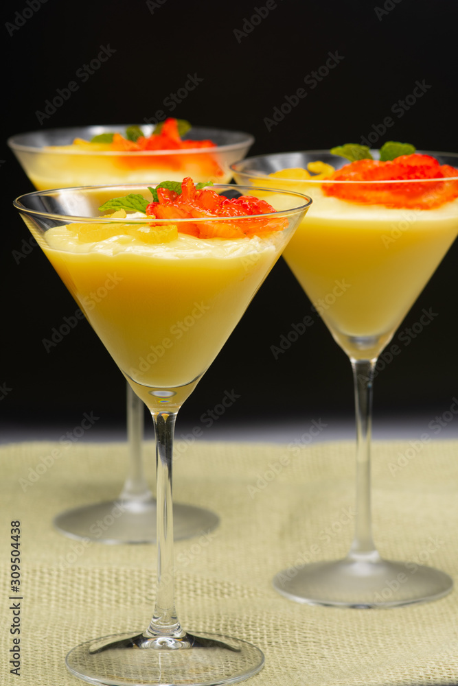 Vanilla Pudding with lemon and strawberry garnish in Martini glass with black background.