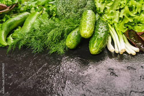 A mixture of fresh produce on a dark table. Dill  green pepper  parsley  cucumbers  broccoli  onions  borax leaves.