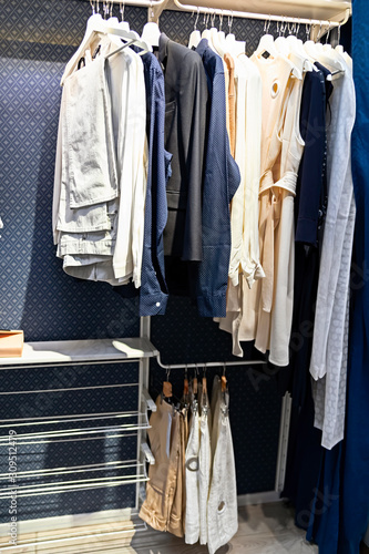 A number of different clothes hang on hangers in a modern blue closet.