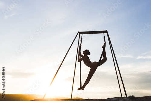 Slim woman practicing fly dance acrobatic yoga poses in hammock outdoors at sunset. Sports and wellbeing concept. Healthy lifestyle.
