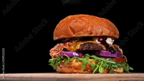 Craft burger is cooking on black background. Consist: sauce, arugula, tomato, red onion, bacon, red currant sauce, ricotta cottage fresh cheese, air bun and marble meat beef. Not made ideal. Looks