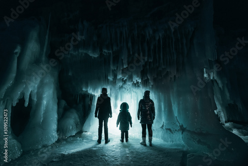 Surreal landscape with people exploring mysterious ice grotto cave. Outdoor adventure. Family exploring huge icy cave, dark majestic landscape. Magical silhouettes on background of illuminated ice photo