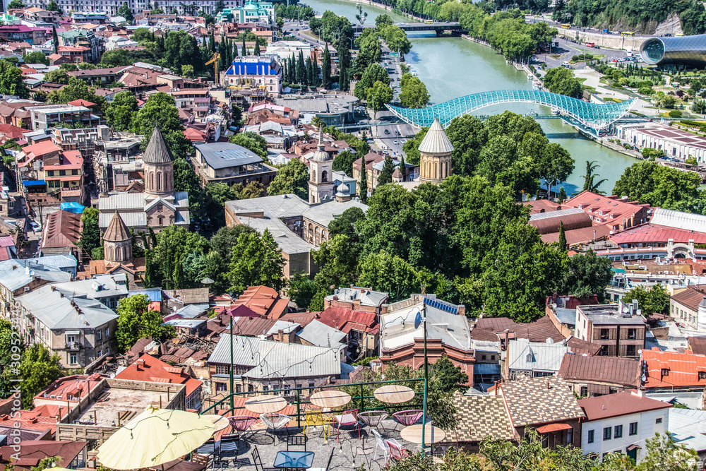Roofs of Tbilisi old town below scenic sidewalk cafe perched on side of mountain near fortress with River Kura and Peace Bridge and cathedrals below