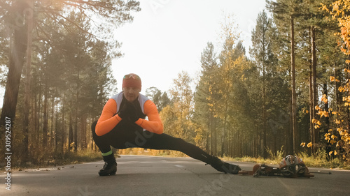 Training an athlete on the roller skaters. Biathlon ride on the roller skis with ski poles, in the helmet. Autumn workout. Roller sport. Adult man riding on skates. The athlete does the workout. photo