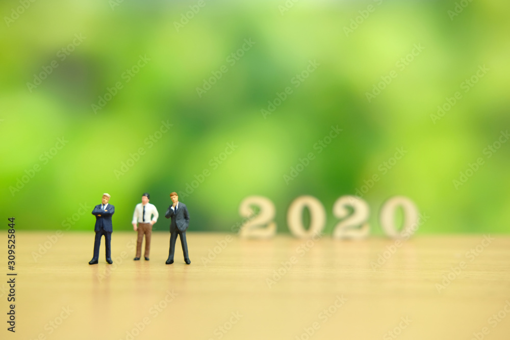 Miniature people - businessman greeting for happy new year 2020 with dreamy green background