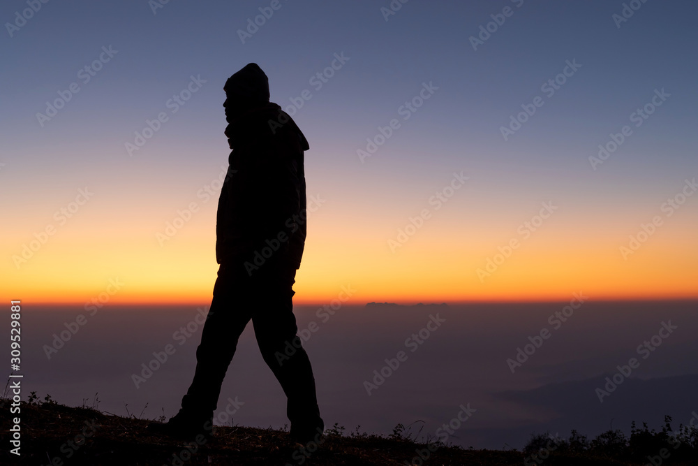 Silhouette man stands alone looking colorful sky in evening time.