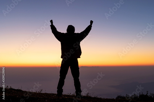 young successful man hiker silhouette with open arms on morning foggy mountain peak.