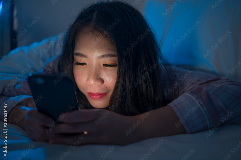 young beautiful and happy sweet Asian Korean woman with in pajamas enjoying with mobile phone app in bed at night in internet social media addiction concept young beautiful and happy sweet Asian Korean woman with in pajamas enjoying with mobile phone app in bed at night in internet social media addiction concept