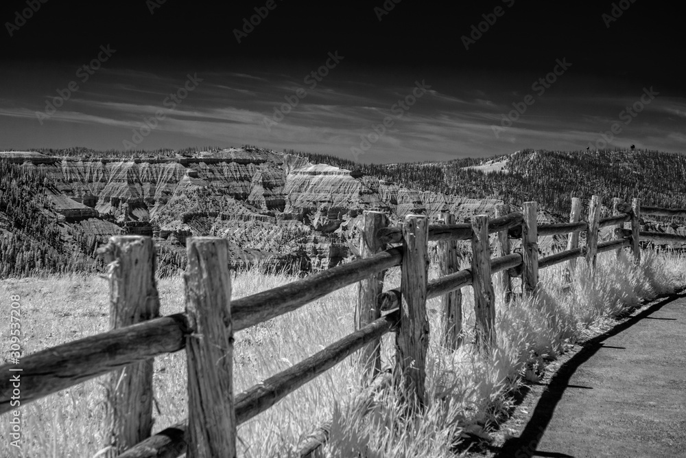 Wooden fence with field and rocky canyon view beyond.