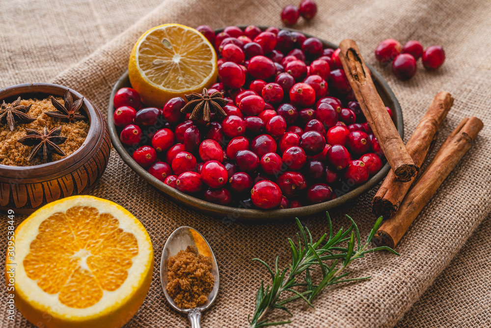 Cranberries on a plate with some ingredients. Lemon, rosemary, anise, cinnamon close up on rustic background Cranberries on a plate with some ingredients. Lemon, rosemary, anise, cinnamon close up on rustic background
