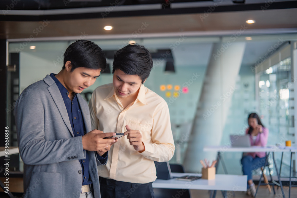 Two young business men are watching something on a mobile phone at work Two young business men are watching something on a mobile phone at work