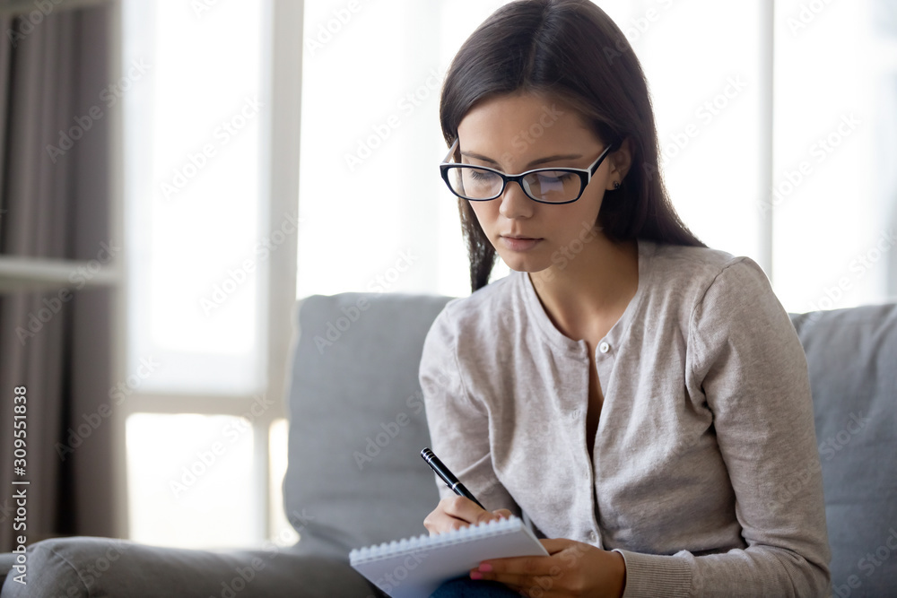 Focused young woman in glasses make notes in notebook Focused young woman in glasses make notes in notebook