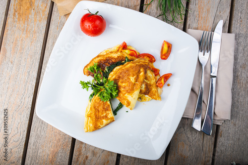 Traditional omelet with vegetables, spinach, tomatoes and herbs on a wooden table in a restaurant.
