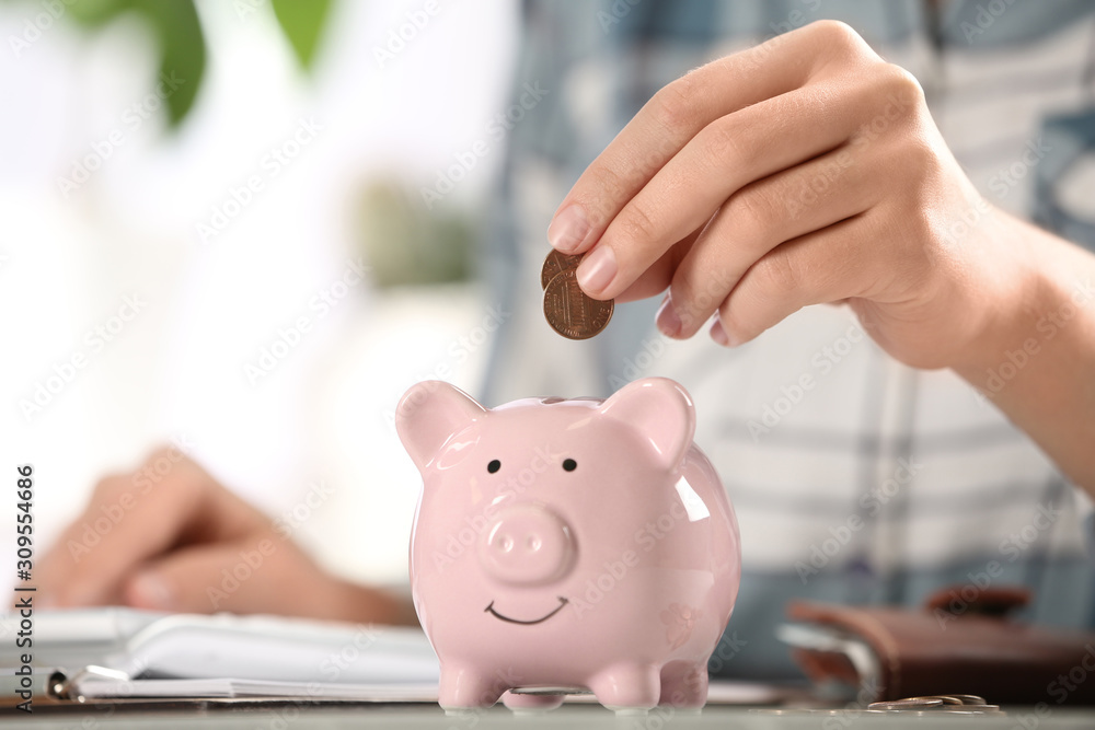 Woman putting money into piggy bank at table, closeup Woman putting money into piggy bank at table, closeup