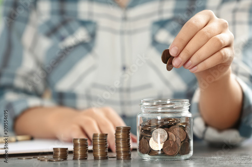 Woman putting money into glass jar at table, closeup