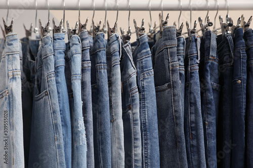 Rack with stylish jeans on color background, closeup