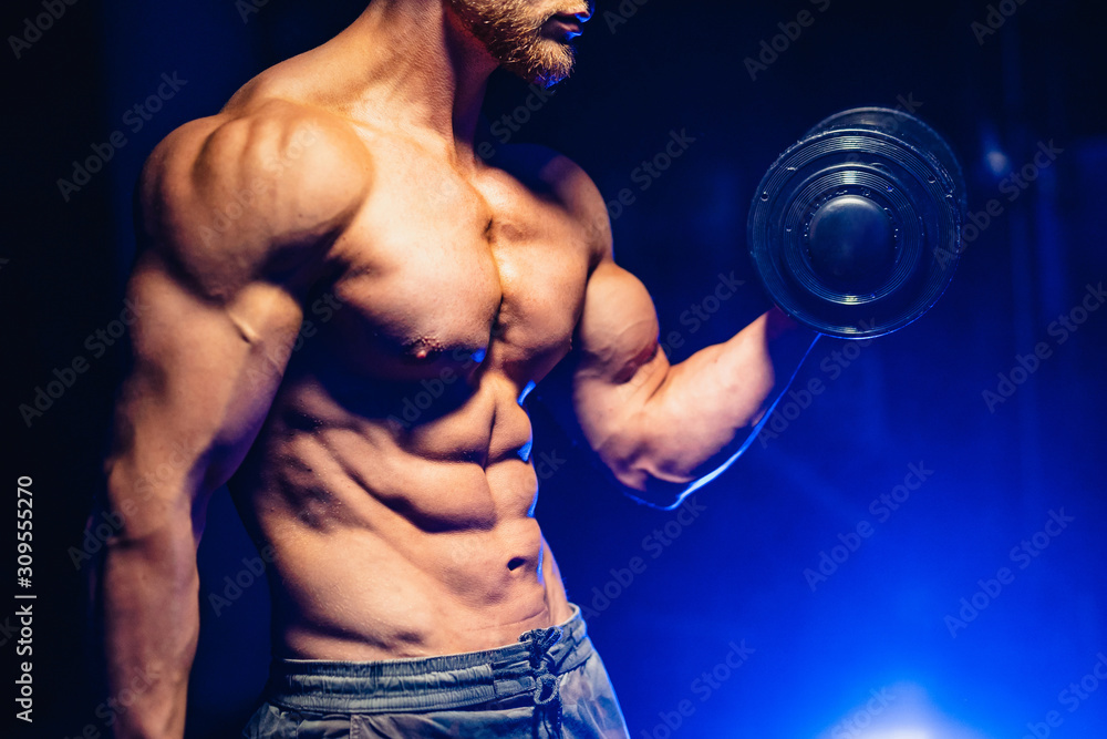 Young handsome sportsman bodybuilder weightlifter with an ideal body, with naked torso poses in front of the camera, abdominal muscles, biceps triceps. Closeup