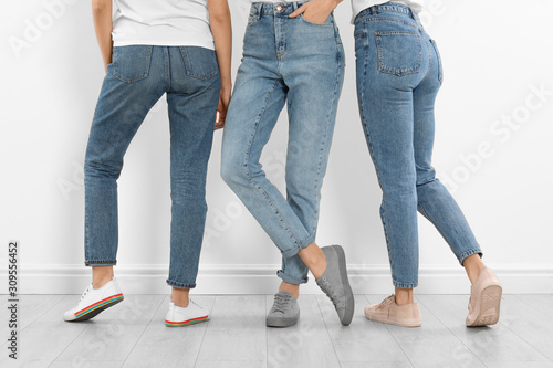 Group of young women in stylish jeans near white wall, closeup