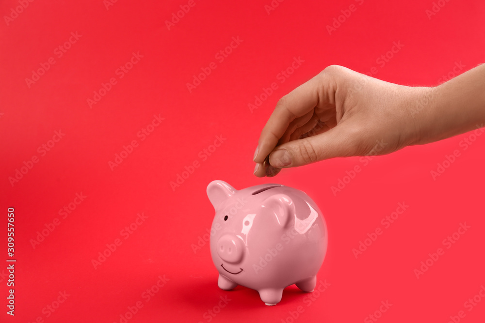 Woman putting coin into piggy bank on red background, closeup. Space for text Woman putting coin into piggy bank on red background, closeup. Space for text