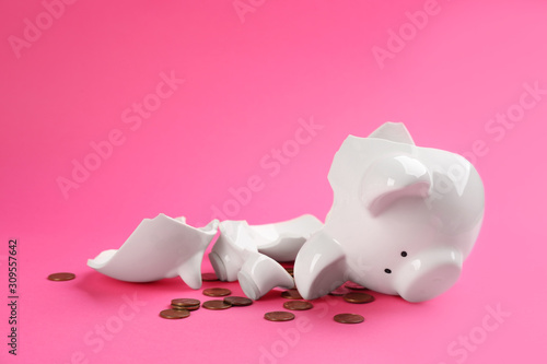 Broken piggy bank with coins on pink background photo
